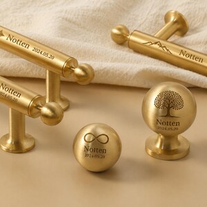 May include: Gold-toned metal hardware with engraved designs. Includes drawer pulls with sound wave and heartbeat patterns, and knobs with tree and infinity symbols. Each piece is marked with "Notten" and the date 2024.05.20.