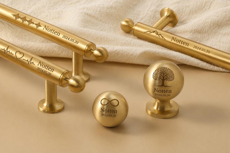 May include: Gold-toned metal hardware with engraved designs. Includes drawer pulls with sound wave and heartbeat patterns, and knobs with tree and infinity symbols. Each piece is marked with "Notten" and the date 2024.05.20.