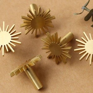 May include: Five gold-toned metal cabinet knobs shaped like stylised suns with a circular centre. The knobs have a textured, slightly raised surface.