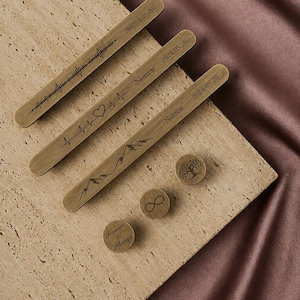 Puede incluir: Recuerdos de madera grabados con varios diseños. Tres piezas largas y delgadas presentan formas de onda grabadas, latidos del corazón y cordilleras, con fechas y el nombre "Notten". Piezas redondas incluyen un símbolo de infinito, un árbol y las palabras "Forever & Always".