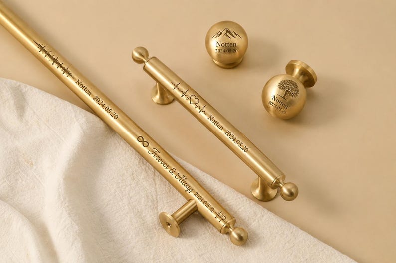 May include: Gold-toned cabinet hardware set, including two handles and two knobs. The handles are engraved with text and symbols, including "Forever & Always" and a heartbeat line. The knobs feature mountain and tree designs.