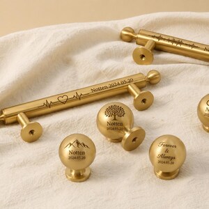 May include: Gold-colored cabinet hardware, including pulls and knobs, with engraved designs and text. The pulls feature a heartbeat line and sound wave pattern. The knobs display a tree, mountains, and infinity symbol. Each piece is inscribed with "Notten 2024.05.20" or "Forever & Always 2024.05.20".