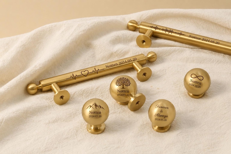May include: Gold-colored cabinet hardware, including pulls and knobs, with engraved designs and text. The pulls feature a heartbeat line and sound wave pattern. The knobs display a tree, mountains, and infinity symbol. Each piece is inscribed with "Notten 2024.05.20" or "Forever & Always 2024.05.20".