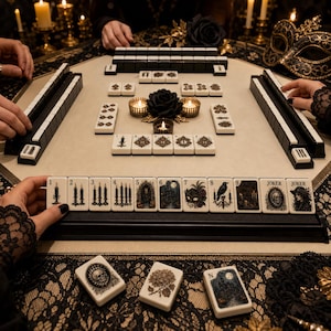 May include: A Mahjong set featuring off-white tiles with intricate black and gold gothic-themed illustrations, including candles, skulls, ravens, and masks. The set includes numbered tiles from one to nine, Joker tiles, and a black tile rack.