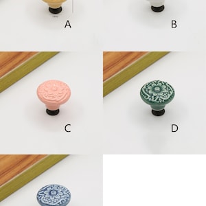 Op de afbeelding: Vijf keramische kastknoppen met bloemmotieven in verschillende kleuren. De knoppen hebben een diameter van 32 mm en een basis van 16 mm. De kleuren zijn goud, wit, roze, groen en blauw.