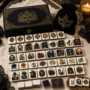 May include: A black rectangular storage box with gold filigree and a mask illustration, a matching black velvet drawstring pouch, and a set of rectangular game tiles featuring various illustrations including skulls, pumpkins, flowers, and masks.