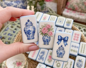Op de afbeelding: Drie rechthoekige witte tegels met afgeronde hoeken, elk voorzien van blauw-witte porseleinmotieven. Eén tegel toont een gemberpot, een andere een vaas met roze rozen, en de derde een blauwe strik boven een kleine gemberpot, met blauwe randen.