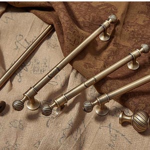 May include: A selection of antique brass cabinet pulls and handles. The hardware features a ribbed ball design and a round base. The pulls are arranged on a textured, neutral-toned fabric.