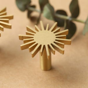 May include: Two gold metal sunburst-shaped cabinet knobs with a round base.