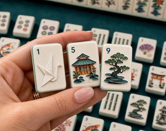 May include: Three rectangular mahjong tiles with light green edges held in a hand. The tiles feature a white origami crane with the number 1, a detailed Japanese building with the number 5, and a green bonsai tree with the number 9.