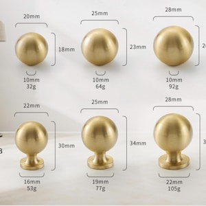 K&ouml;nnte beinhalten: Eine Auswahl an goldfarbenen Schrankkn&ouml;pfen in verschiedenen Gr&ouml;&szlig;en. Die Kn&ouml;pfe sind kugelf&ouml;rmig oder haben eine kugelf&ouml;rmige Oberseite mit einem Sockel. Die Ma&szlig;e sind in Millimetern und Gramm angegeben, wobei der gr&ouml;&szlig;te Knopf 28 mm Durchmesser und 37 mm H&ouml;he misst.