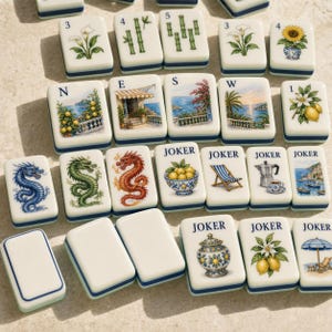 May include: A collection of rectangular mahjong tiles featuring various illustrations including dragons, flowers, coastal scenes, and the word JOKER. The tiles are white with blue borders and display detailed colorful graphics.