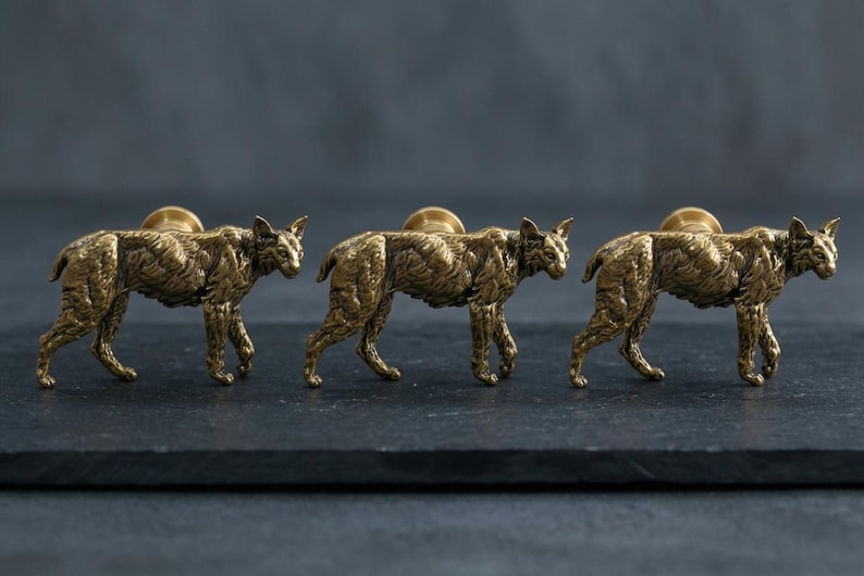 May include: Three brass-toned cabinet knobs shaped like walking bobcats. Each knob features a detailed, textured metallic finish depicting the feline's fur, ears, and tail, with a circular mounting base attached to the center of each animal figure.