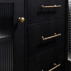 May include: Close-up of a black wooden cabinet with three drawers and a side cabinet. The cabinet has gold-coloured handles and knobs. The side cabinet has a glass door with vertical lines.