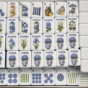May include: A set of white rectangular Mahjong tiles arranged in a box, featuring blue and green illustrations of flowers, dragons, flags, and various objects. Each tile displays specific text labels like Flower, Joker, Red, Soap, and Green.