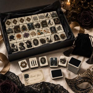 May include: A set of rectangular mahjong tiles featuring intricate illustrations of skulls, candles, ravens, flowers, and masquerade masks. The tiles are presented in a black box with a matching black velvet drawstring pouch and a thank you card.
