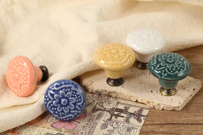 Op de afbeelding: Vijf keramische kastknoppen met bloemmotieven in verschillende kleuren, waaronder roze, geel, wit, blauw en groen. De knoppen hebben een vintage stijl en zijn perfect om elke woning een vleugje elegantie te geven.
