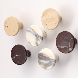 Può includere: Un set di sei pomelli circolari per mobili con diverse texture in pietra naturale. Il set comprende due pomelli in travertino beige poroso, due pomelli in marmo marrone scuro con venature bianche e due pomelli in marmo bianco con venature.