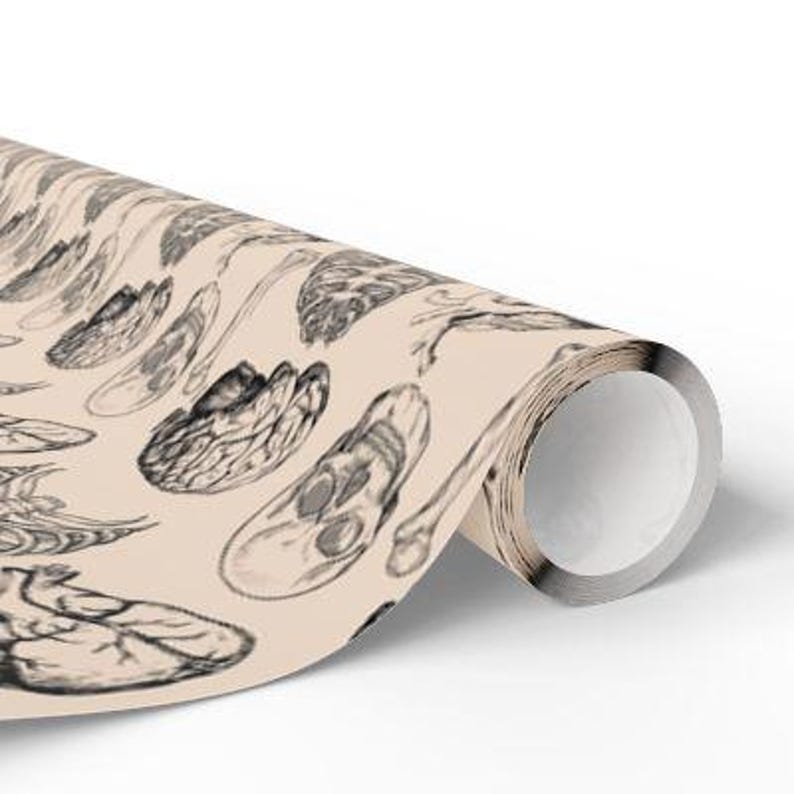May include: A beige wrapping paper with a repeating pattern of black and white anatomical illustrations. The illustrations include bones, skulls, and wings.