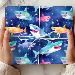 May include: Blue wrapping paper with a repeating pattern of colorful cartoon sharks. The sharks are in various poses, including swimming, jumping, and smiling. The background is a dark blue with white stars.