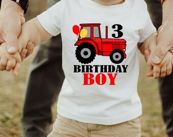 May include: White short-sleeved t-shirt featuring a red tractor graphic with the number 3, two balloons, and the text "BIRTHDAY BOY" in black and red. The shirt is worn by a child.