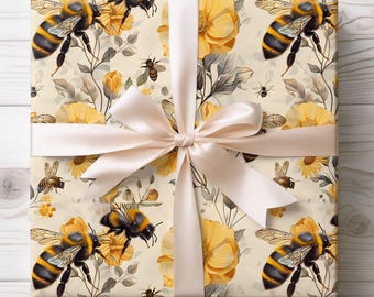 May include: Gift wrap featuring a repeating pattern of yellow and black bees, yellow flowers, and gray leaves on a cream background. A cream-colored satin ribbon is tied in a bow around the wrapped package.