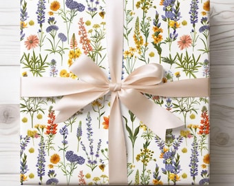 May include: A wrapped gift with white floral patterned wrapping paper featuring colorful wildflowers in orange, yellow, purple, and pink. A light peach satin ribbon is tied in a bow around the gift.