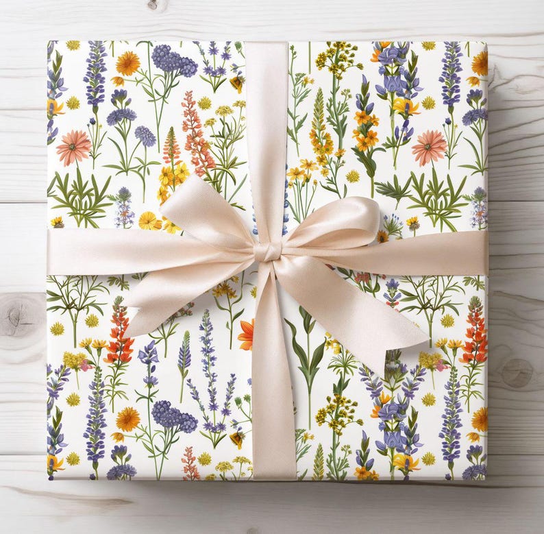 May include: A wrapped gift with white floral patterned wrapping paper featuring colorful wildflowers in orange, yellow, purple, and pink. A light peach satin ribbon is tied in a bow around the gift.