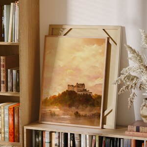May include: A framed painting of a castle in a misty landscape. The castle is surrounded by trees and the sky is a soft yellow and pink.