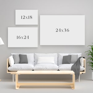 May include: Three blank rectangular canvases with the dimensions 12x18 inches, 16x24 inches, and 24x36 inches are displayed on a gray wall. The canvases are above a white sofa with gray pillows and a wooden coffee table.