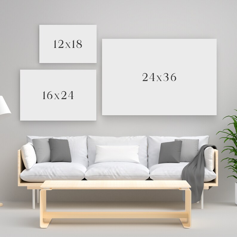May include: Three blank rectangular canvases with the dimensions 12x18 inches, 16x24 inches, and 24x36 inches are displayed on a gray wall. The canvases are above a white sofa with gray pillows and a wooden coffee table.