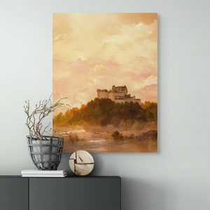 May include: A painting of a castle on a hill with a misty river in the foreground. The sky is a soft orange and pink.