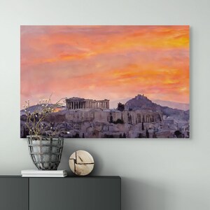 May include: A canvas print of the Acropolis in Athens, Greece, under a vibrant orange and pink sunset. The ancient Greek architecture is depicted in shades of gray and beige, set against a colorful sky. The print is displayed above a dark gray cabinet.