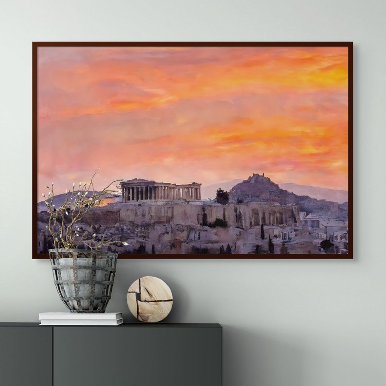 May include: Framed print of the Acropolis in Athens, Greece, under a vibrant sunset sky. The artwork features the ancient structures in shades of gray and beige, set against a backdrop of orange and pink clouds. The frame is a dark brown.