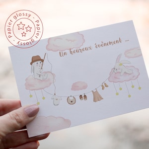 May include: A baby shower card with a charming illustration. It depicts a bunny fishing from a cloud, with baby clothes strung on a line. The text "Un heureux événement" is printed in gold, with a glossy finish.