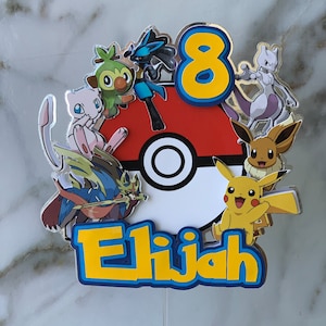 Puede incluir: Un adorno para pastel de Pok&eacute;mon colorido con una Pok&eacute;bola roja y blanca, un n&uacute;mero 8 amarillo y varios personajes de Pok&eacute;mon, incluyendo Pikachu, Eevee y Grookey. El adorno tambi&eacute;n incluye el nombre "Elijah" en letras amarillas.