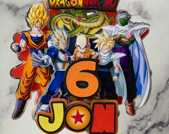 Op de afbeelding: Een kleurrijke Dragon Ball Z-taarttopper met Goku, Vegeta, Piccolo, Gohan en Krillin. De topper bevat het nummer 6 en de naam "JON" met een Dragon Ball Z-logo.