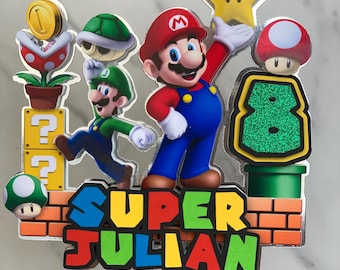 Könnte beinhalten: Ein Tortendekor mit Mario und Luigi Figuren aus dem Super Mario Bros. Videospiel. Das Dekor enthält einen grünen Stern, einen roten Pilz, ein grünes Rohr und eine Mauer aus Ziegeln. Der Text "SUPER JULIAN" ist in bunten Buchstaben geschrieben.