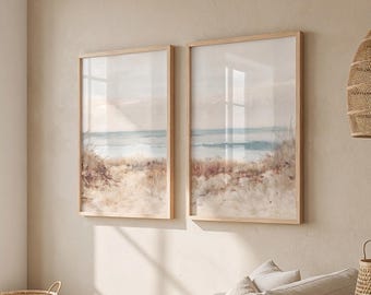May include: Two rectangular wall art prints in light wood frames featuring a watercolor landscape of a sandy beach with dunes and a calm blue ocean horizon. The artwork displays soft beige, tan, and muted blue tones in a vertical orientation.