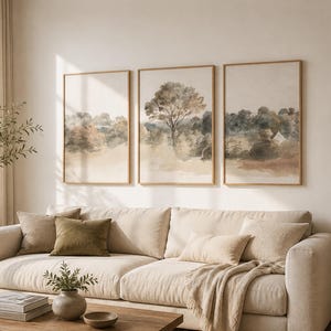 May include: A living room with a beige sofa, cushions, and a wooden coffee table. Three framed landscape paintings are displayed above the sofa. A large window with curtains and a bookshelf add to the room's neutral colour scheme.