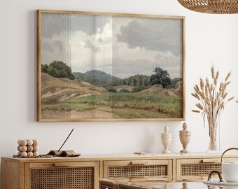 May include: A framed landscape painting depicts a serene countryside scene with rolling hills, green fields, and a cloudy sky. The artwork is displayed above a wooden cabinet with woven panels, enhancing the room's aesthetic. The word "AQUAMARINE" is visible at the bottom.