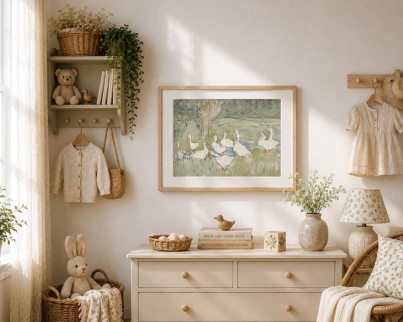 May include: A cozy nursery scene with a framed watercolor painting of geese, a woven basket, and a plush bunny. A light-colored dresser, a lamp, and a small shelf with a teddy bear and books complete the room's decor.