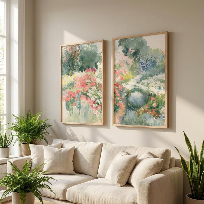 May include: Two framed watercolor paintings depict a garden scene with pink, white, and yellow flowers, and green foliage. The paintings are in light wood frames and hang above a beige sofa. Ferns and other plants are in the foreground.