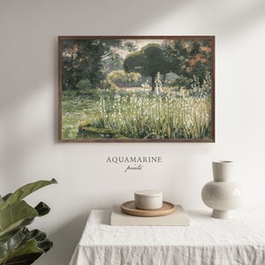 Pu&ograve; includere: Una stampa incorniciata raffigurante un paesaggio di giardino con fiori bianchi, vegetazione lussureggiante e alberi. L'opera d'arte ha un'estetica vintage, con una cornice in legno marrone. Il testo "AQUAMARINE prints" &egrave; stampato in basso nell'immagine.