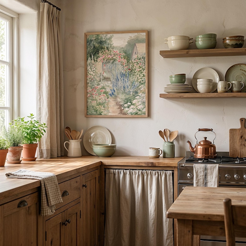 May include: A kitchen scene with wooden cabinets, shelves, and a table. A framed watercolor painting of a garden hangs on the wall. Copper kettle on the stove. Various ceramic bowls, plates, and mugs are displayed. Potted herbs sit on the countertop near a window.