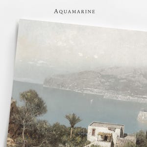 May include: A print with the word "AQUAMARINE" at the top, depicting a coastal scene with a body of water, mountains, and buildings. The artwork has a muted colour palette.