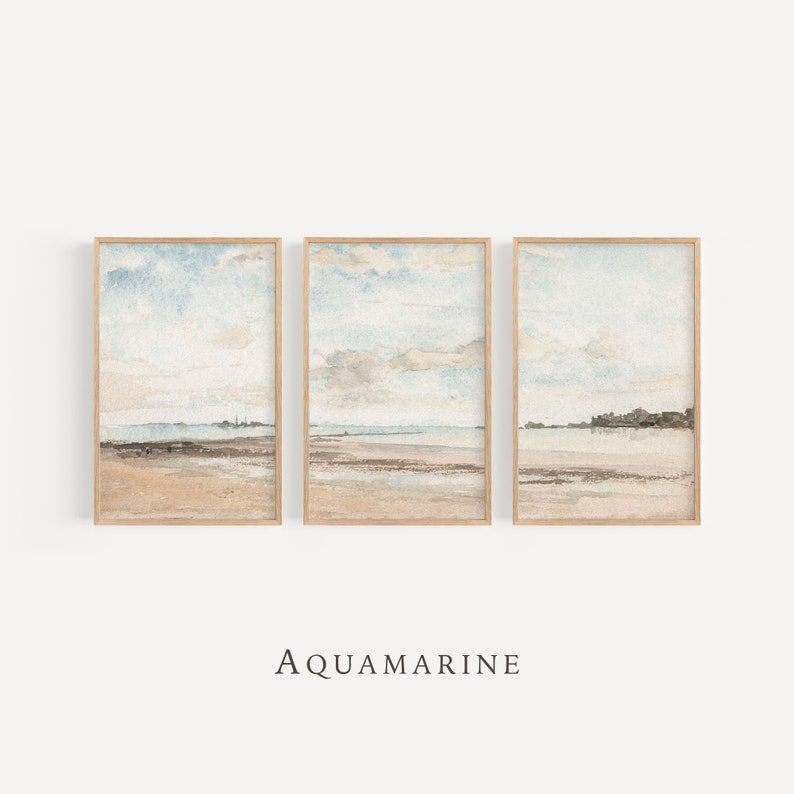 May include: Three framed watercolor prints depicting a serene beach scene with a light blue sky and beige sand. The artwork is in a vertical orientation and features a minimalist aesthetic. The text "AQUAMARINE" is printed at the bottom.