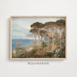 May include: A framed landscape print titled AQUAMARINE featuring a coastal scene with tall pine trees on a grassy cliff overlooking a blue sea and distant mountains under a cloudy sky. The artwork is enclosed in a light-coloured wooden frame.
