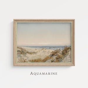 May include: A framed watercolor print of a beach scene. The artwork depicts sand dunes, ocean waves, and a pale sky. The frame is a light wood color, and the text "AQUAMARINE" is printed at the bottom.