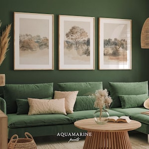 May include: Three framed landscape prints in neutral tones hang above a green velvet sofa. The prints depict trees and fields in a watercolour style. A round wooden coffee table and decorative items complete the scene.